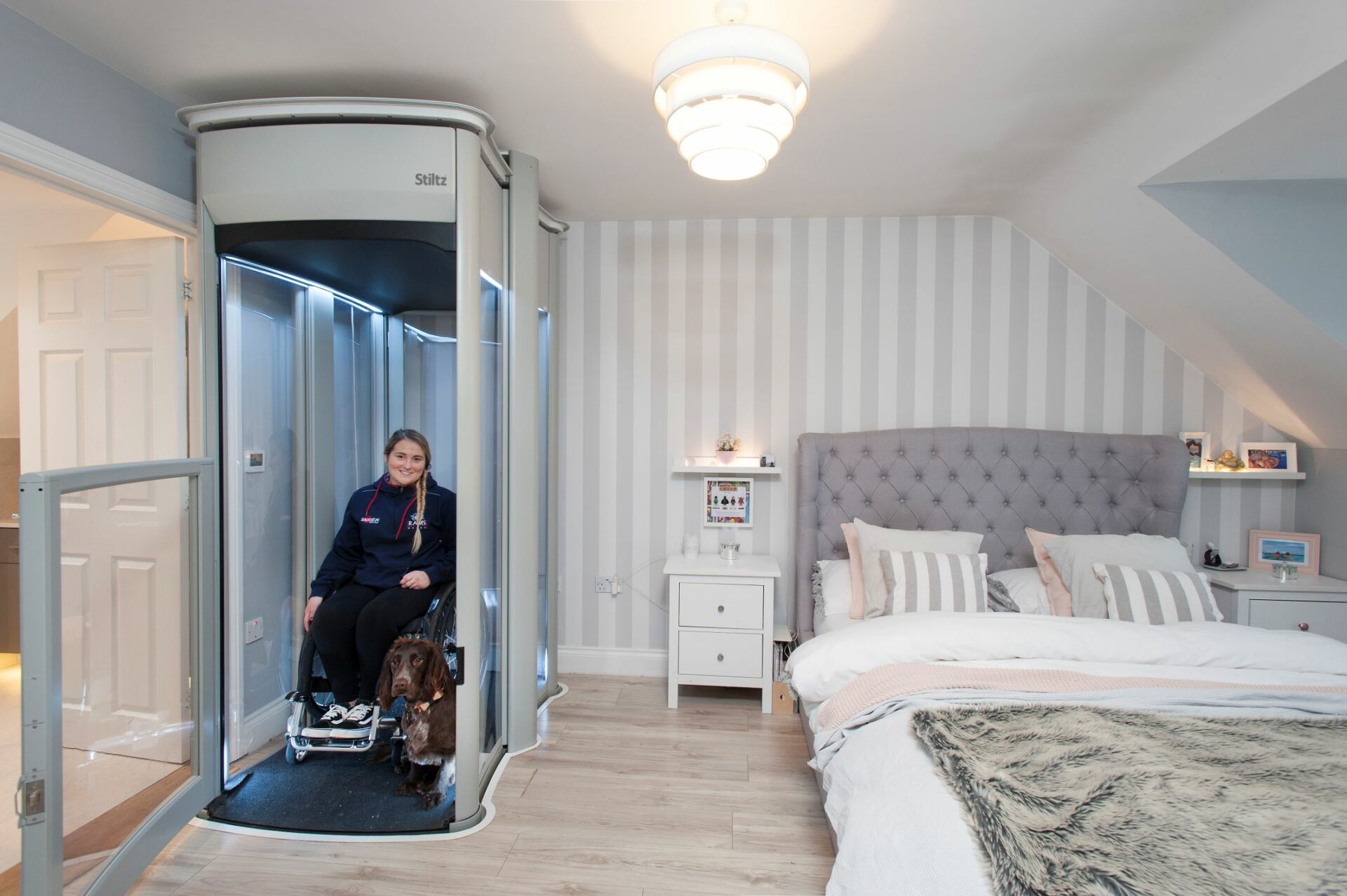 Wheelchair user using a through-floor home lift in a bedroom, showing step-free access and a spacious platform.
